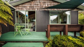 Una casa moderna con fachada de madera, ventanas grandes y una terraza verde con mobiliario exterior.
