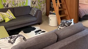 Una habitación acogedora con un sofá gris, una escalera de madera y un muro decorado con motivos de vaca en verde y blanco.