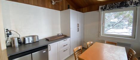 A compact kitchen with white cabinets, a wooden countertop, and a dining table with chairs.