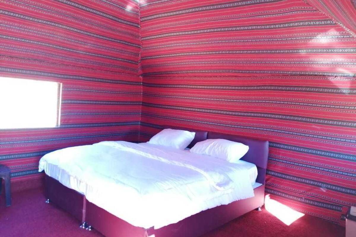 A room with a bed, a window, and red patterned walls.
