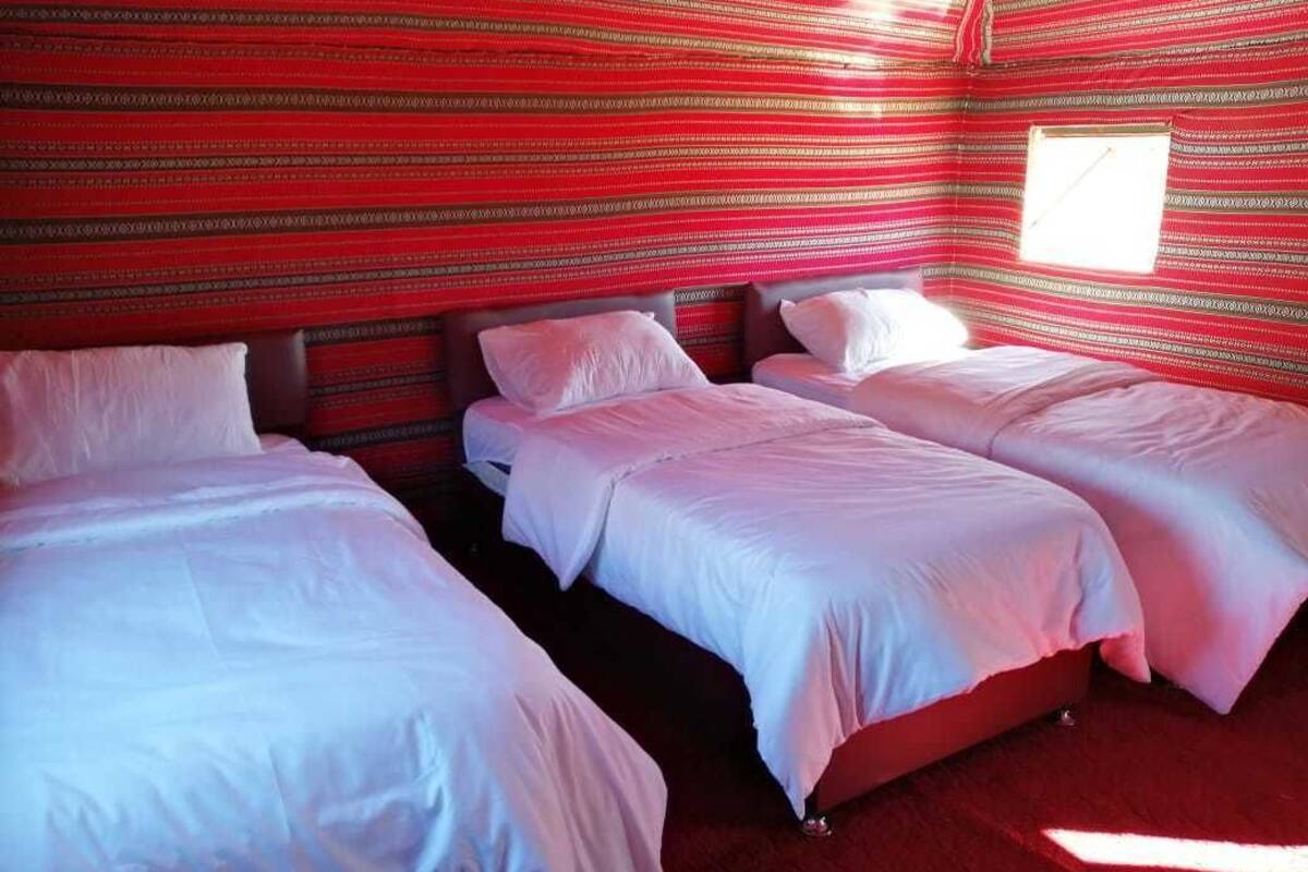 A room with three beds aligned against a red patterned wall, a window, and a red carpet.