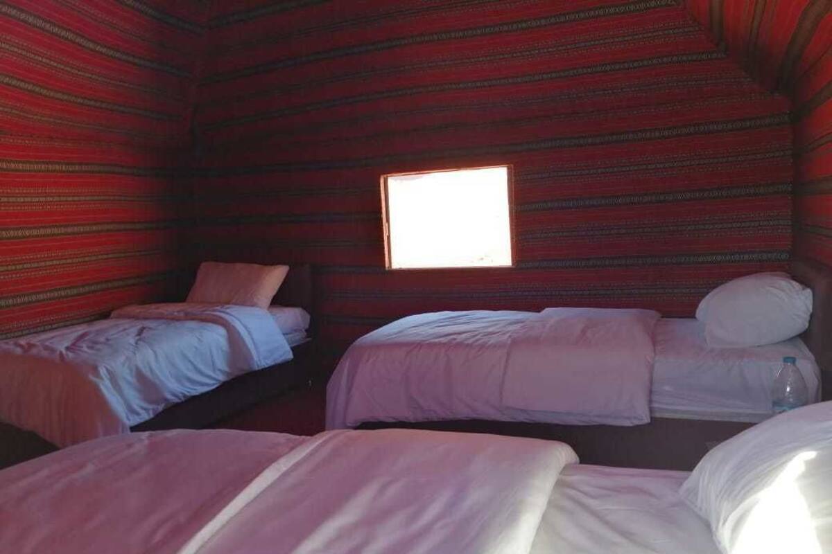 A room with three beds, a window, and a red patterned wall.