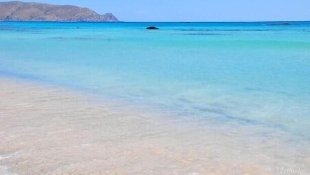 Une plage bordée d’une eau turquoise et cristalline, avec une montagne qui se profile à l’horizon.