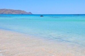 Een strand met helder turquoise water en een berg in de verte.