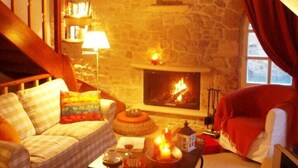 Un salon chaleureux avec un mur en pierre, une cheminée, un canapé, un fauteuil rouge et une table basse décorée de bougies.