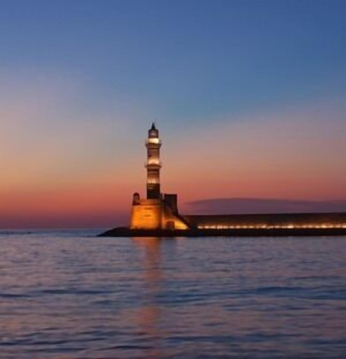 Un phare au coucher du soleil, avec une eau calme au premier plan.
