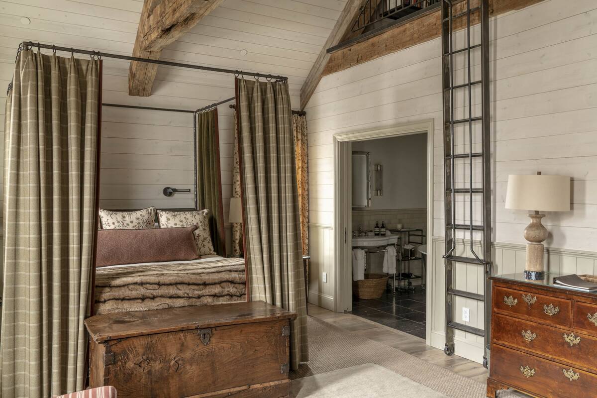 A four-poster bed with a wooden chest of drawers and a dresser with floral handles. A ladder leads to an upper level.