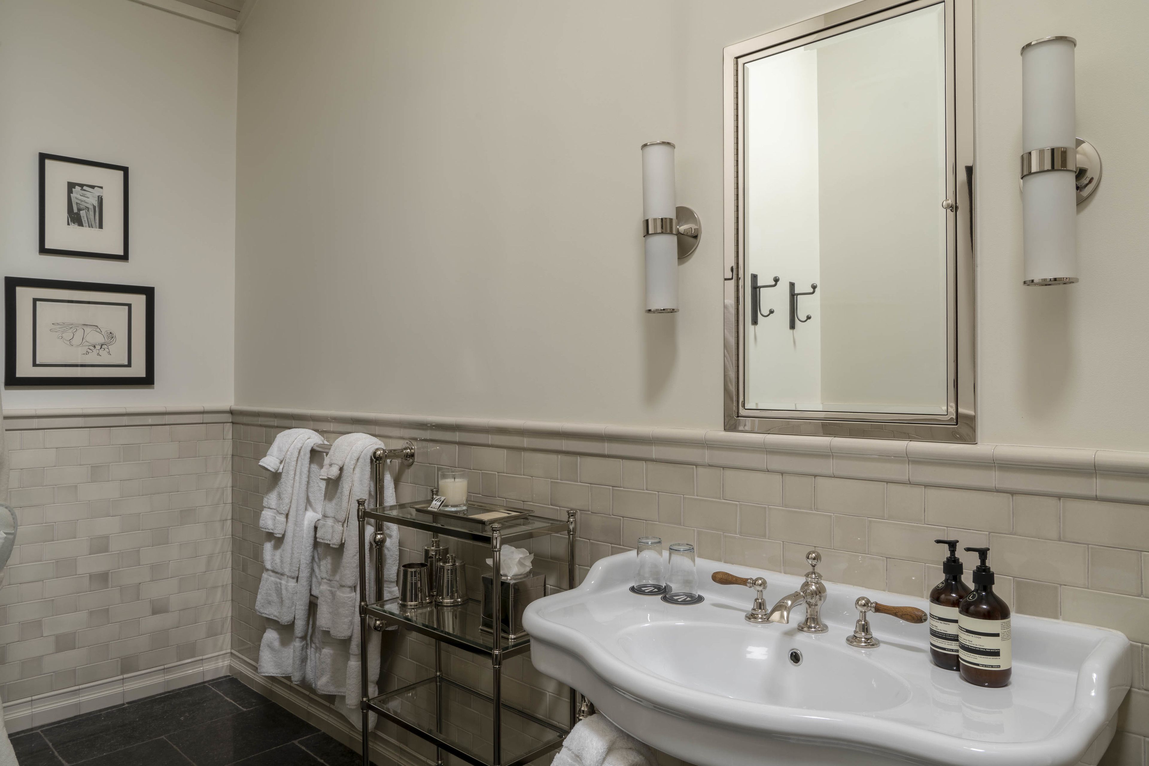 A bathroom with a white sink, two wall-mounted lights, a mirror, and a towel rack with towels.