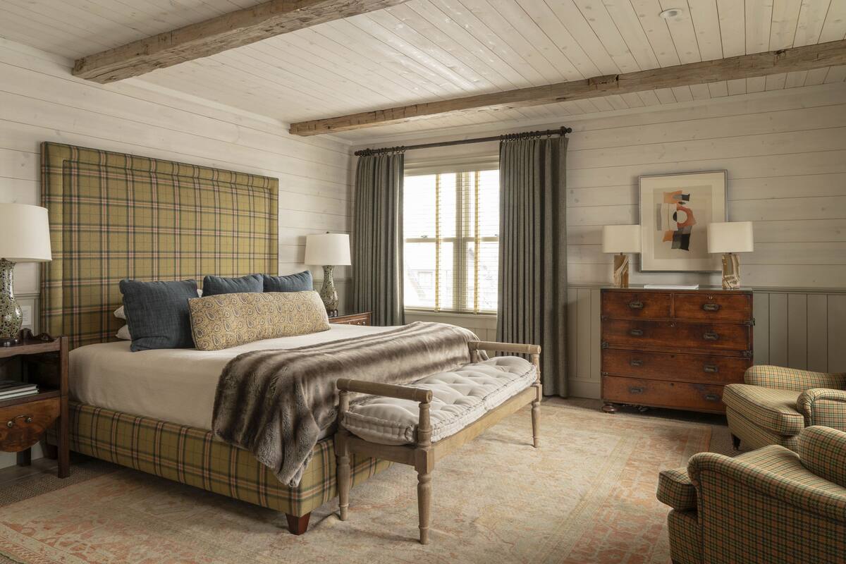 A bedroom with a large bed, a bench, a dresser, and a chair.