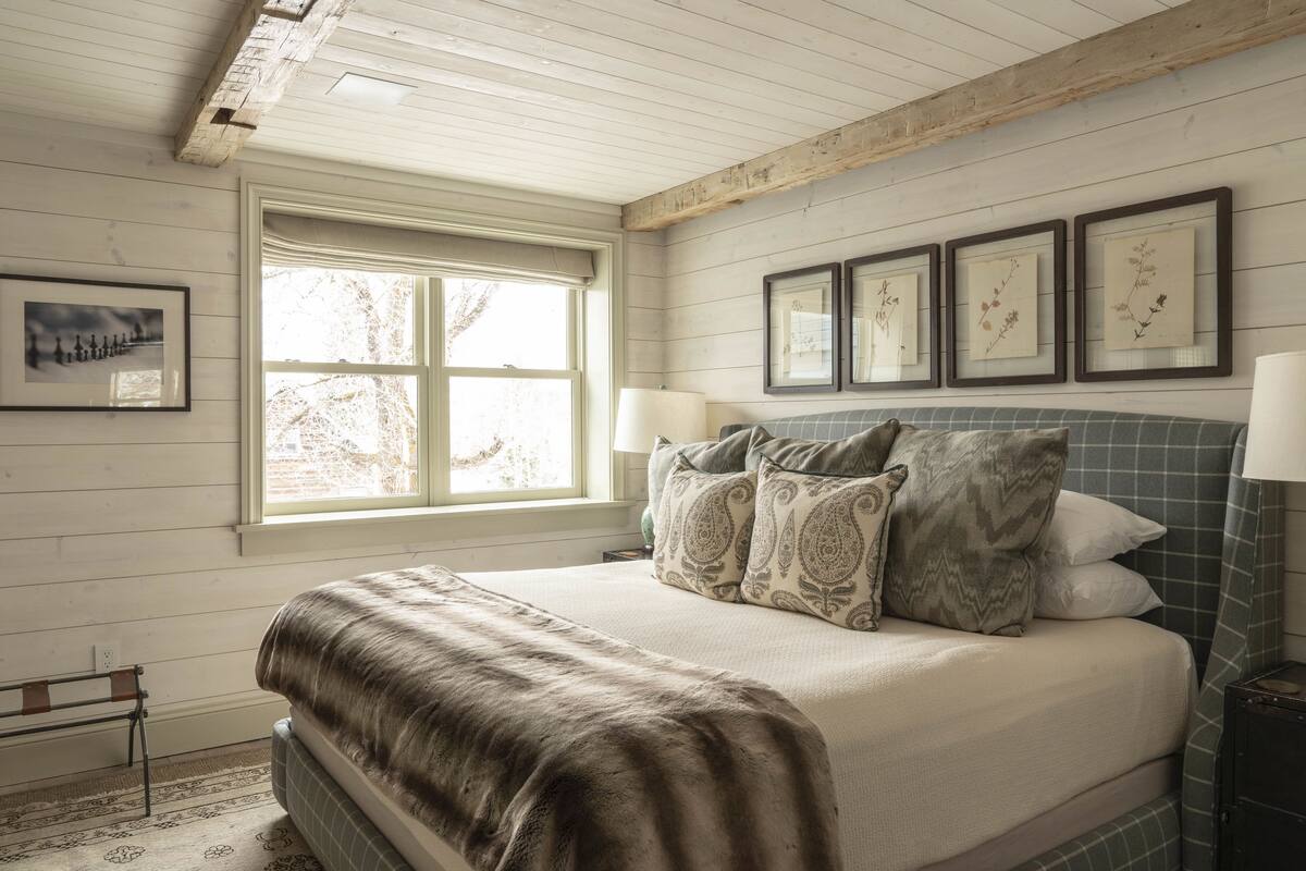 A bedroom with a large bed, a window, and framed botanical prints on the wall.