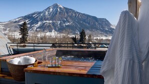 A wooden deck with a hot tub, a wicker basket, and a clear glass bottle. - Eleven Scarp Ridge Lodge (Crested Butte)