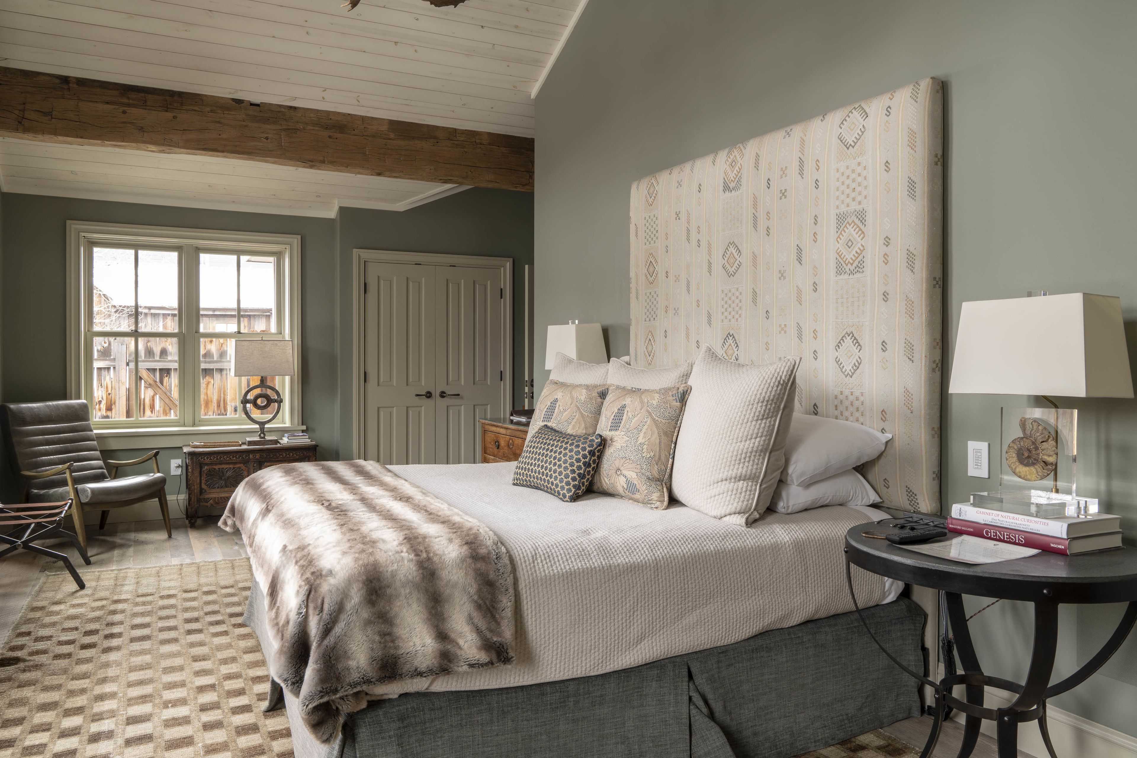 A bedroom with a large bed, a desk, a chair, a lamp, and a view of the outside.