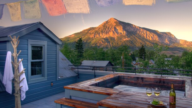 A rooftop terrace with a hot tub, wooden table, and two glasses of wine. - Eleven Scarp Ridge Lodge (Crested Butte)