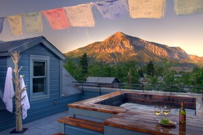 A rooftop terrace with a hot tub, wooden table, and two glasses of wine.