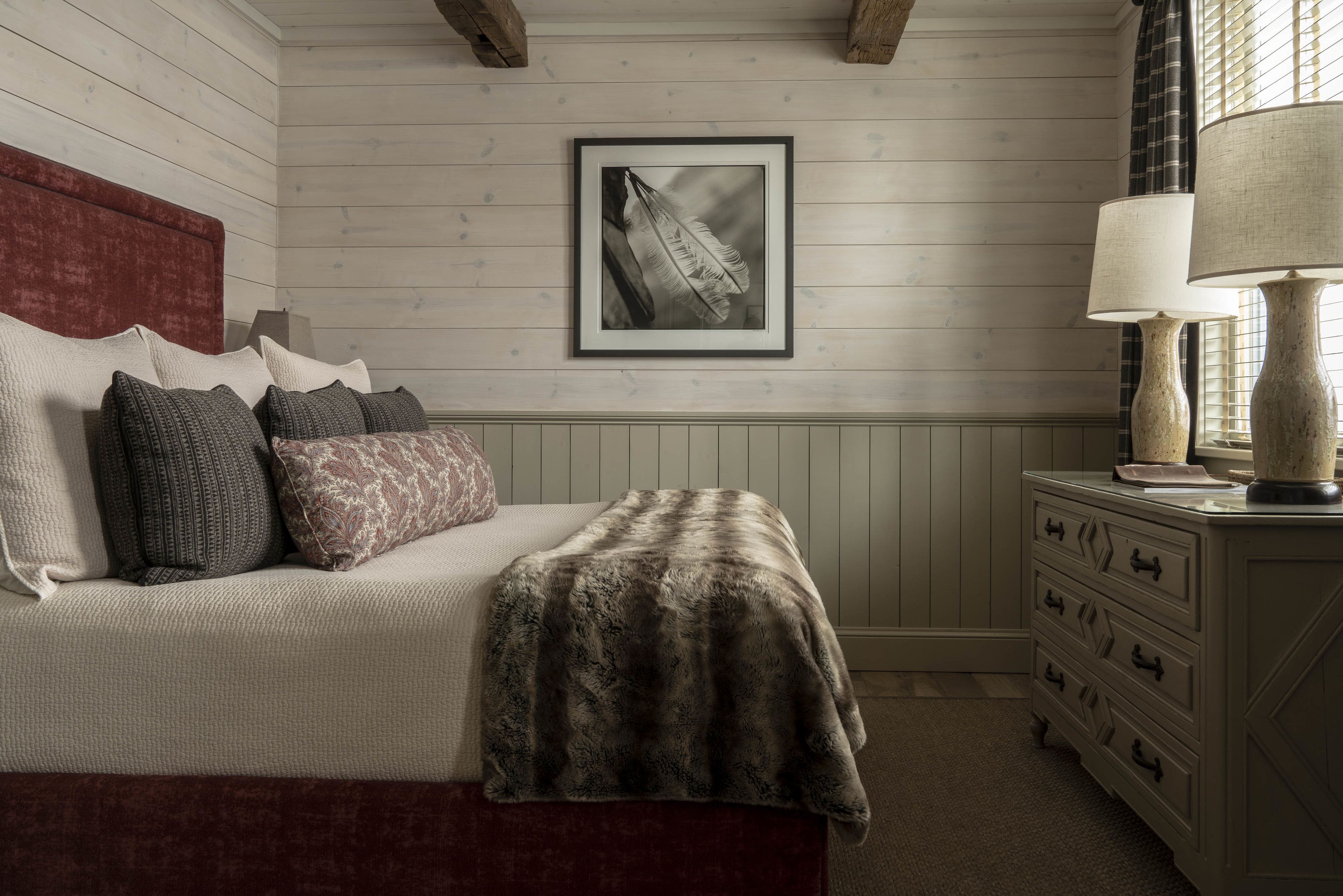 Une chambre à coucher avec un lit, des oreillers, un tableau encadré au mur, une commode et une lampe.