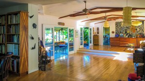 A spacious living room with a wooden floor, a ceiling fan, and a dining area with chairs and a table. - Gingerhill Farm Retreat (Kealakekua)