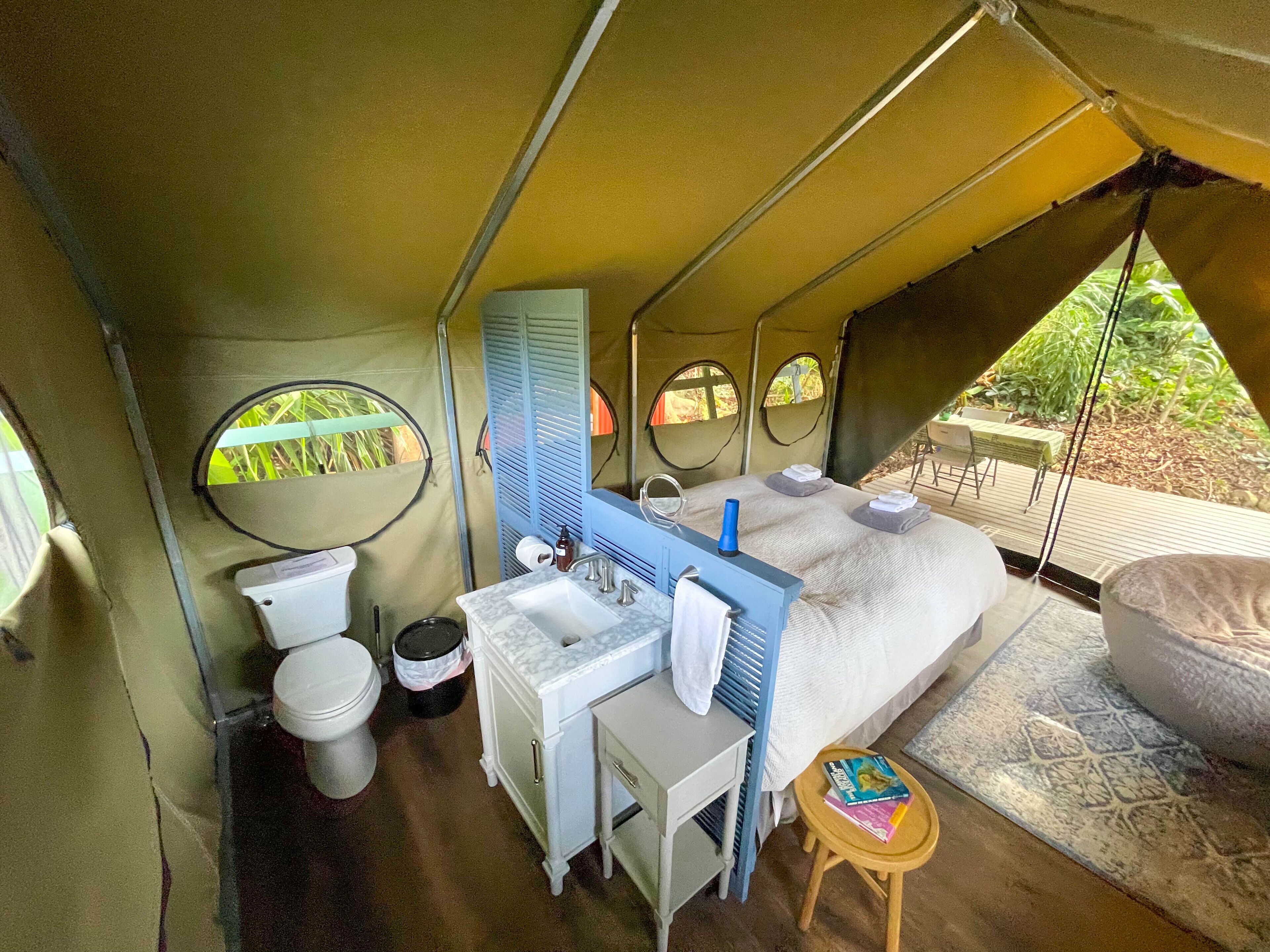 Habitación tipo alojamiento con carpa, cama, mesita, lavabo e inodoro.