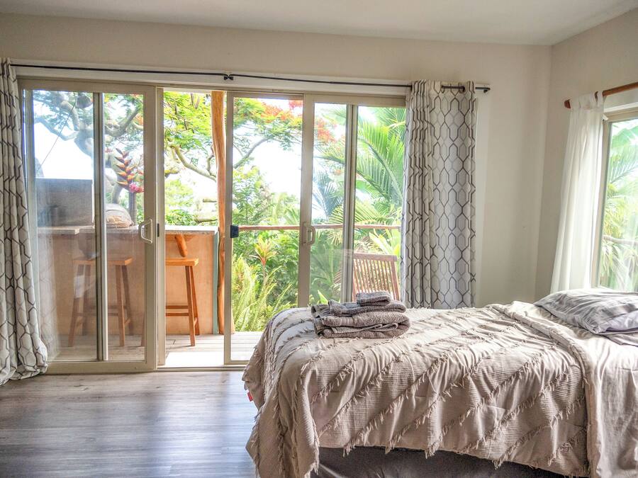 Un dormitorio con cama, una silla y vistas a un balcón con plantas.