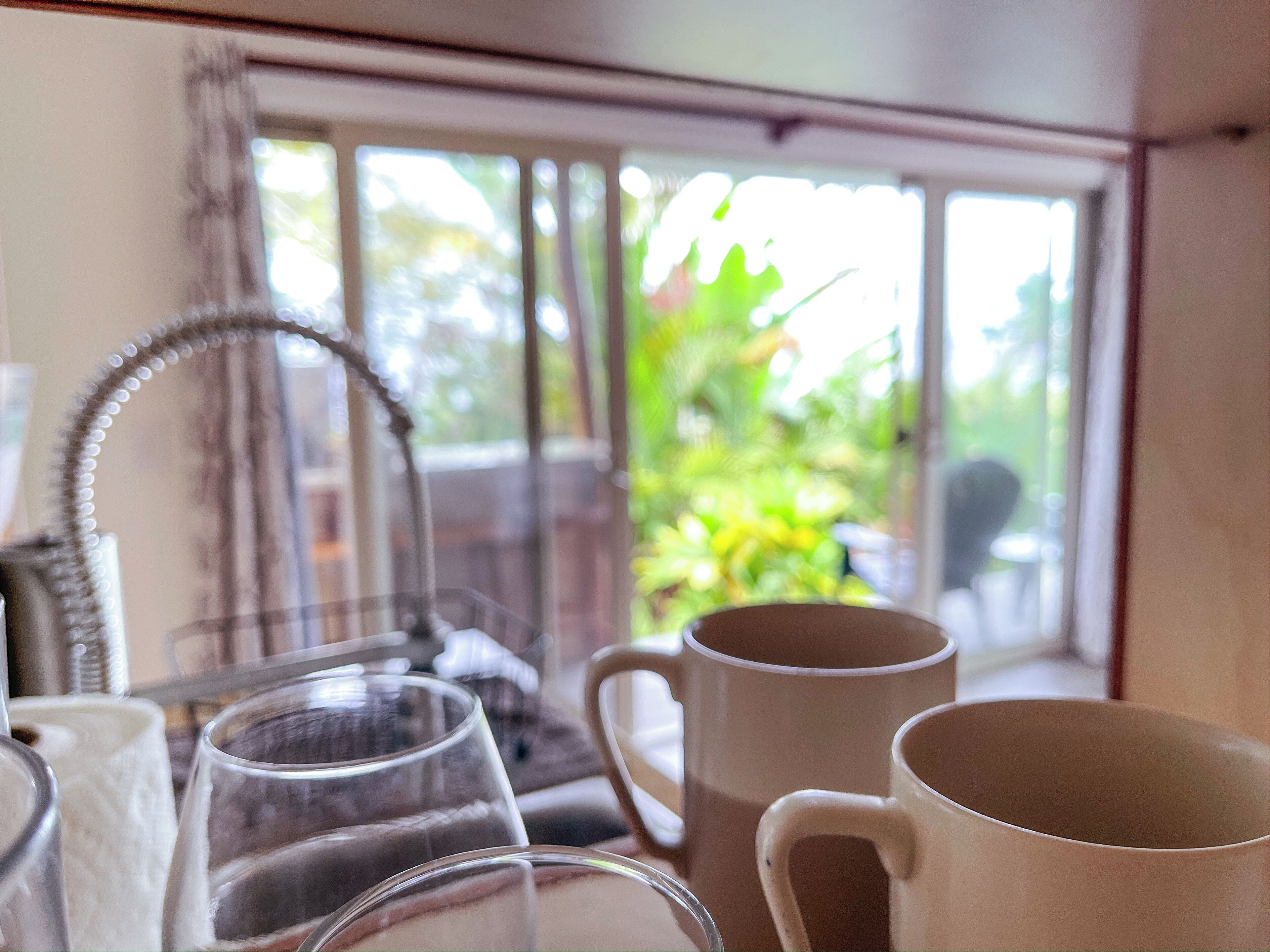 Une pièce avec une fenêtre donnant sur un espace verdoyant, une chaise, ainsi que plusieurs tasses et verres disposés sur une table.