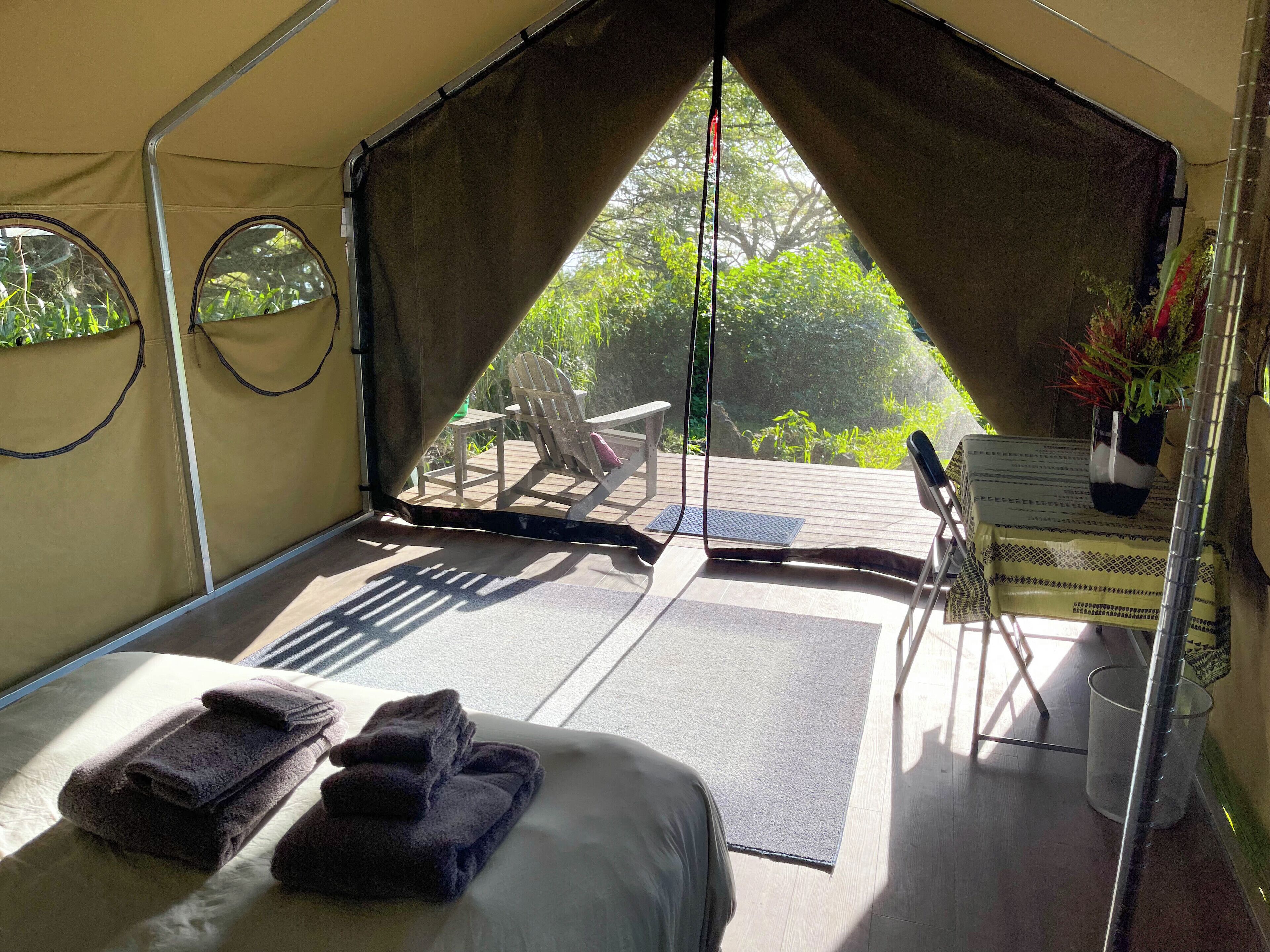 A tented accommodation with a bed, towels, a table with a plant, and a chair.