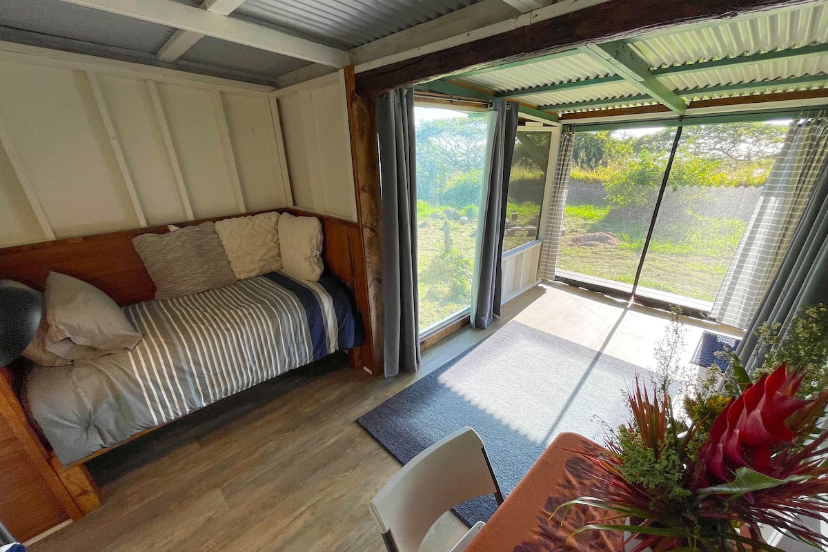 Een gezellige kamer met een bed, een tafel met een bloevas en uitzicht op groen buiten.