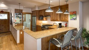 Une cuisine moderne dotée de plans de travail en granit, d’appareils électroménagers en acier inoxydable, d’armoires en bois et de tabourets de bar.