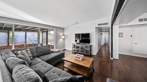 Un salon moderne avec un canapé d’angle gris, une table basse en bois et un téléviseur posé sur un meuble.