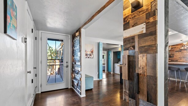 Un intérieur moderne avec un plancher en bois, une porte en verre donnant sur l’extérieur et un espace cuisine visible à travers une porte ouverte.