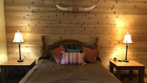 Una stanza con rivestimento in legno, un letto, due comodini con lampade e una testata in legno.