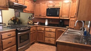 Una cucina con pensili in legno, un piano cottura in acciaio inossidabile, un forno a microonde e un lavello.