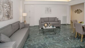 A modern living room with a grey sofa, a coffee table, and a dining area with a table and chairs. - Roomy & Comfortable Apt Near Acropolis by GHH (Athens)