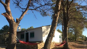 Un edificio bianco con un muro in pietra, un'amaca tra gli alberi e un cane nelle vicinanze.