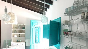 Una stanza con una porta color petrolio, un armadietto bianco e mensole con bicchieri.