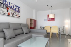 Een moderne woonkamer met een grijze bank, een glazen salontafel, een eethoek met gele stoelen en een rode kast.
