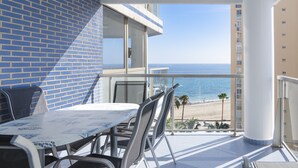 Een balkon met een tafel en stoelen, met uitzicht op een strand en de oceaan.