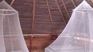 Une chambre avec deux lits, chacun doté d’une moustiquaire, des poutres en bois et un plafond en bois.