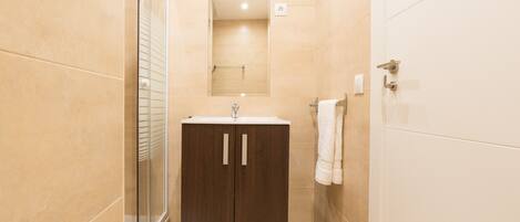 A modern bathroom with a glass shower enclosure, a dark wooden cabinet with a sink, and a mirror above it.