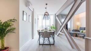 Un espace de salle à manger moderne avec une table dressée pour quatre personnes, un luminaire suspendu et un escalier menant à un autre niveau.