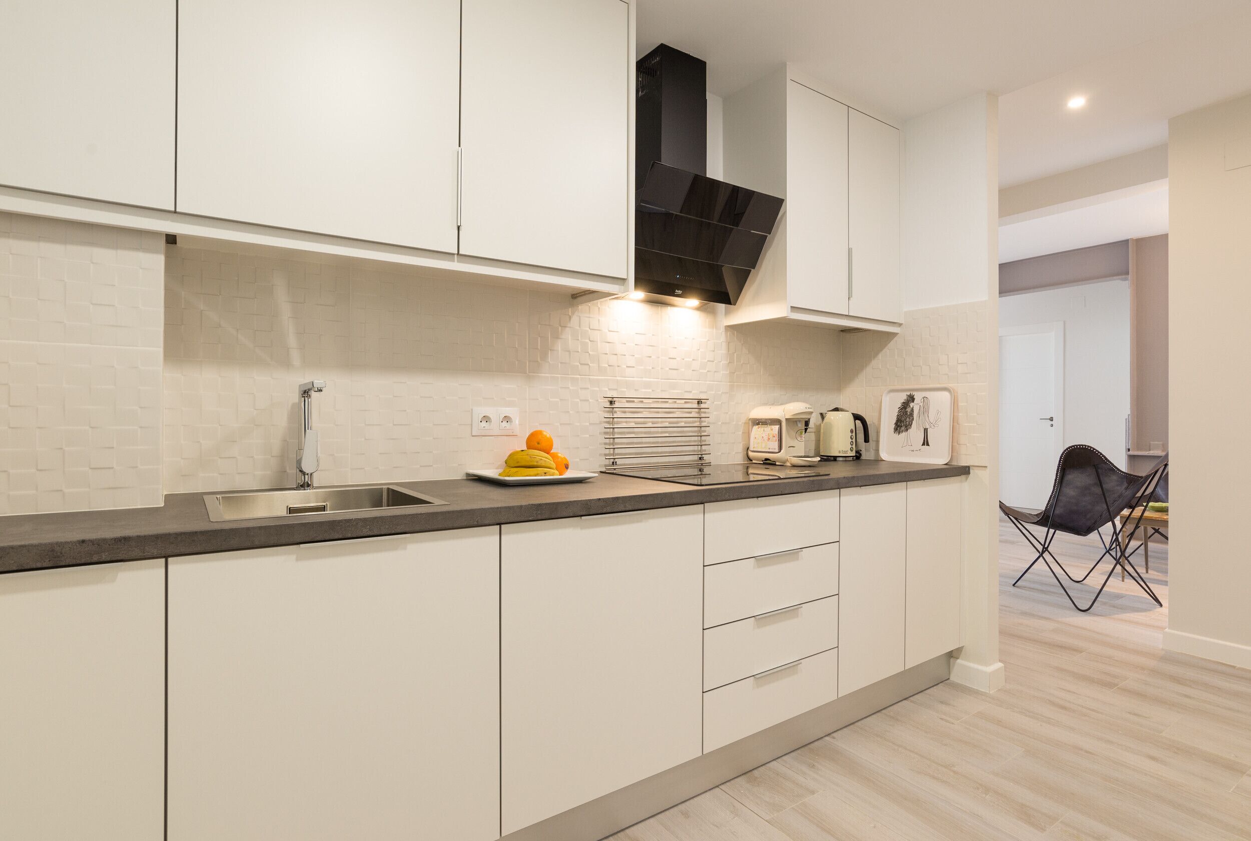 Una cocina moderna con gabinetes blancos, un lavamanos de acero inoxidable y una campana extractora negra.