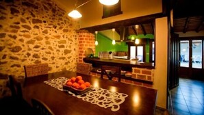 A rustic dining area with a stone wall, wooden table, and a fruit bowl. - Rural house (Las Mimbres house 1) 10 people Rivera n 4 (Fuentes de Béjar)