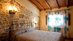 A bedroom with a stone wall, a bed with a patterned bedspread, a nightstand, and a wall-mounted lamp. - Rural house (Las Mimbres house 1) 10 people Rivera n 4 (Fuentes de Béjar)