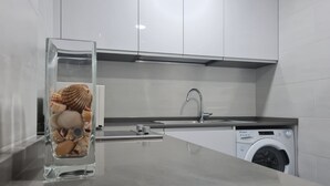 A modern kitchen with a stainless steel sink, a built-in washing machine, and a glass vase with seashells. - MalagaSuite Wonderful Sunset Torremolinos (Torremolinos)
