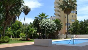 A swimming pool area with a tiled deck, surrounded by palm trees and a building with balconies. - MalagaSuite Wonderful Sunset Torremolinos (Torremolinos)