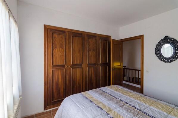 Une chambre avec une grande armoire en bois, un lit avec une literie à motifs et un miroir au mur.