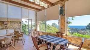 A balcony with a checkered table and chairs, stone walls, and a view of the sea.