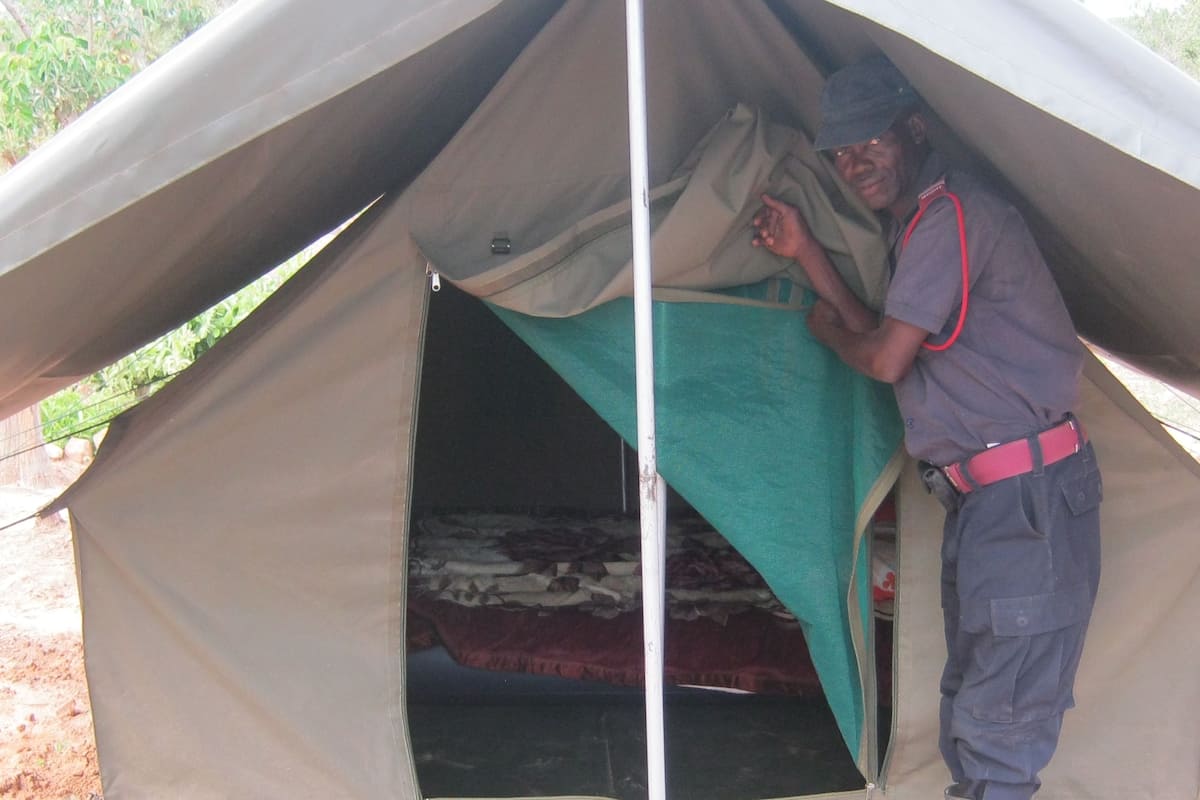 A tent with a single bed inside, a person standing at the entrance, and a red belt around the person's waist.