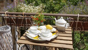 A wooden table set with white dishes, a teapot, and a yellow fruit on a balcony overlooking a lush landscape.
