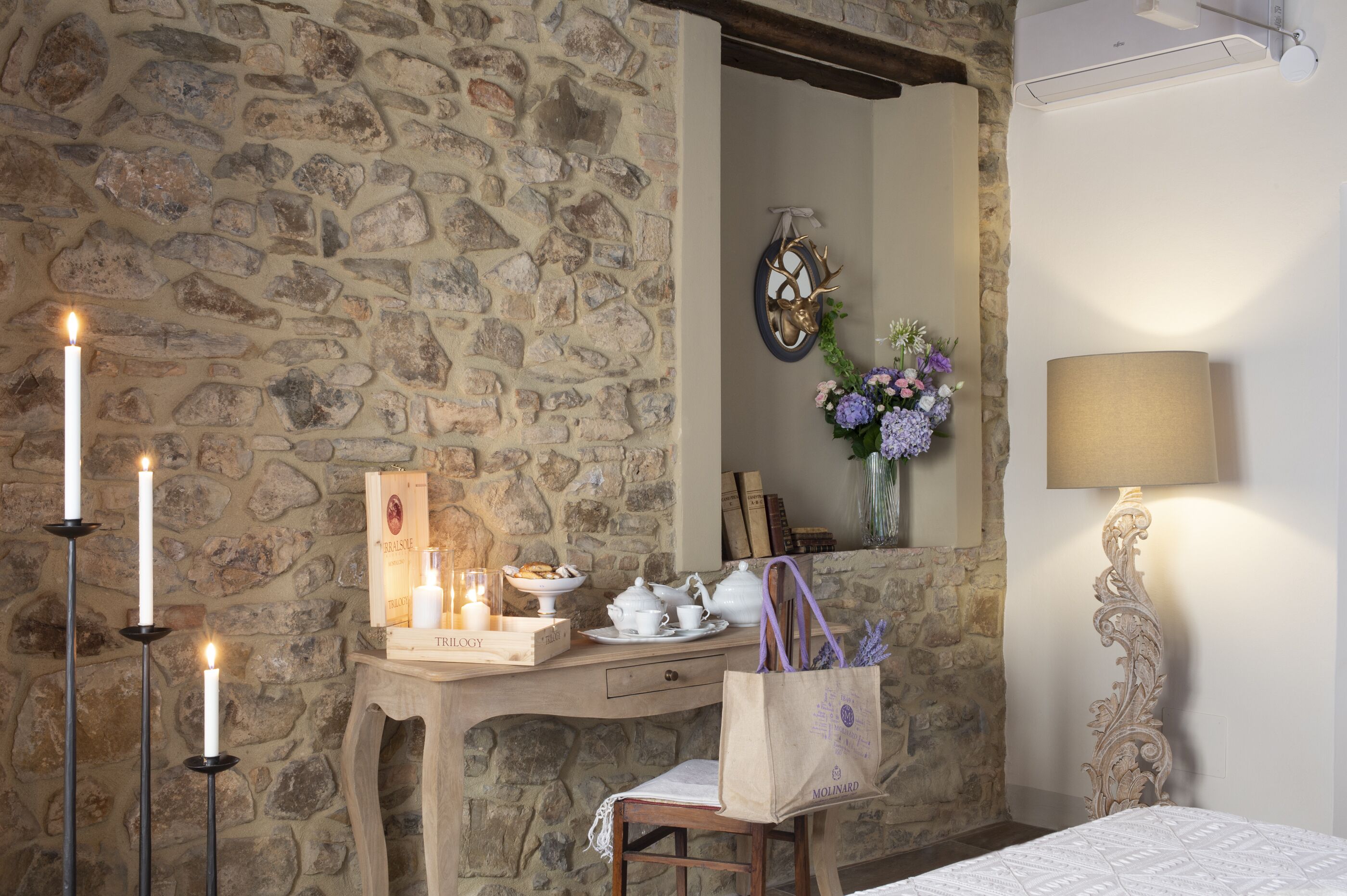 A cozy room with a stone wall, a wooden desk with candles, a mirror, and a lamp.