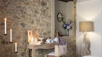 A cozy room with a stone wall, a wooden desk with candles, a mirror, and a lamp.