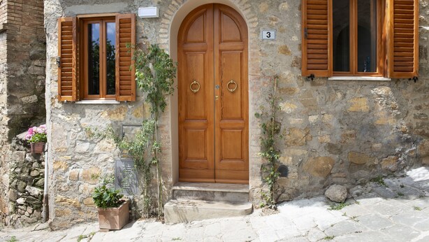 A stone building with a wooden door and two windows with shutters.
